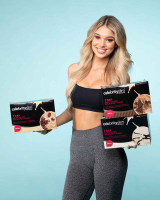 A woman holding up boxes of Celebrity Slim 7 Day Delicious Meal Replacement Shake Cafe Latte, Chocolate, and Vanilla